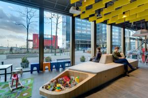 two people sitting on a couch in a room with windows at MEININGER Hotel Amsterdam City West in Amsterdam