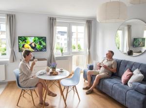 two people sitting on a couch in a living room at Olly Apartament PARKING i BALKON Ciechocinek in Ciechocinek