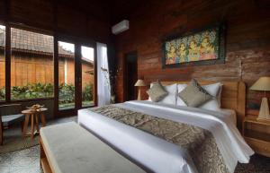 a bedroom with a large white bed in a room with windows at Pondok Kumpi ubud in Ubud
