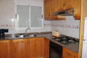 a kitchen with wooden cabinets and a sink and a stove at Villas Los Olivares - Deniasol in Els Poblets