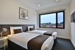 two beds in a hotel room with a large window at Quality Apartments Dandenong in Dandenong