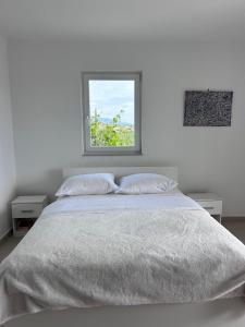 a white bedroom with a bed and a window at Apartment Zekija in Barbat na Rabu