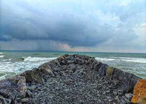 a rock pier on the ocean with a cloudy sky at Koovathur Ecr beach house in Kūvattūr
