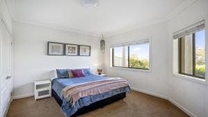 a white bedroom with a bed and two windows at 'Gone Coastal' by HolidayCo in Killcare