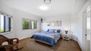 a white bedroom with a bed and a chair at 'Gone Coastal' by HolidayCo in Killcare