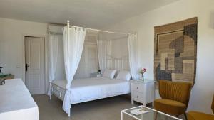 a white bedroom with a canopy bed and a chair at Casa Naya Ibiza in Sant Llorenç de Balafia