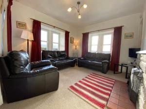 a living room with black leather furniture and red curtains at The Lodge Ellary in Lochgilphead