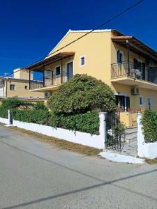 a yellow house with a white fence and bushes at Dimosthenis Apartments in Agios Georgios
