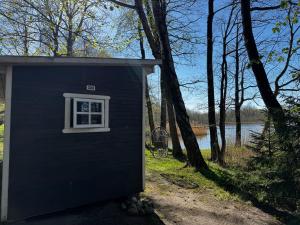 a black out house with a window in front of a lake at The lake house in Mockava