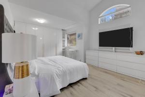 a white bedroom with a bed and a flat screen tv at Guest House in Calgary Downtown in Calgary