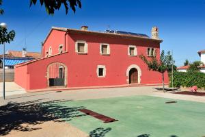 un edificio rosso con un campo verde davanti di Masia Casa Roja a Banyeres del Penedes