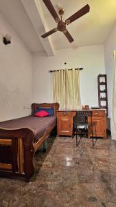 a bedroom with a bed and a desk and a ceiling fan at Manasthala Brindavan in Mysore