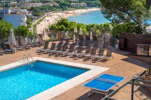 a swimming pool with lounge chairs and a beach at GHT S'Agaró Mar Hotel in Sant Feliu de Guíxols
