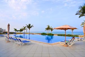 a swimming pool with chairs and an umbrella and the ocean at Wateera Jebel Sifah-Beachfront & Golf View in As Sīfah