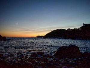 a sunset over the ocean with a rocky beach at Watersreach in Collieston