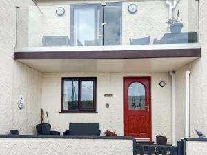 a house with a red door and a balcony at Beach Cottage in Benllech