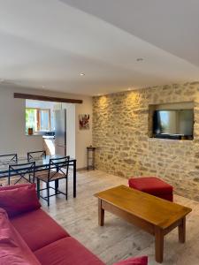 a living room with a couch and a tv on a stone wall at Le Mas des Eglantiers in Propiac
