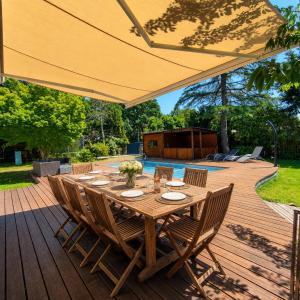 a wooden table with chairs and a large umbrella at Le Chêne Vert - Grande Villa familiale avec piscine - Bassin d'Arcachon in Arès