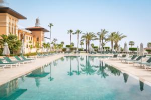 a pool at a resort with chairs and palm trees at The Place Palacio Mojacar & Spa by ALEGRIA Adults Only in Mojácar