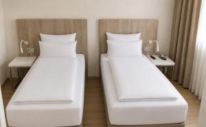 two beds in a hotel room with white pillows at DORMERO Hotel Fürth in Fürth