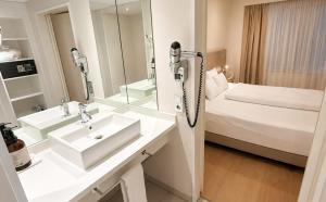 a white bathroom with a sink and a bed at DORMERO Hotel Fürth in Fürth