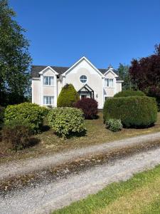 a white house with bushes in front of a road at White House tree view in Drumshanbo