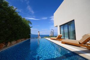 a woman standing next to a swimming pool next to a house at Palmera Dream Vila in Sarandë