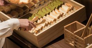 a person is holding a knife in a wooden box of bread at Nesthotel Alt Meguro Ekimae in Tokyo