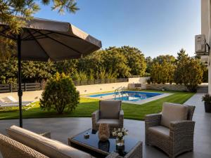 a patio with chairs and an umbrella and a pool at Villa Rose Ground Floor - Private Swimming Pool Garden in Koskinou