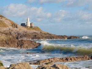 a wave in the ocean with a lighthouse in the background at Fully accessible bungalow by the Beach in Port Talbot