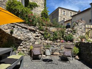a stone wall with two chairs and a table and an umbrella at En si bon chemin - Gîte d'étape chemin 70 in Le Monastier sur Gazeille
