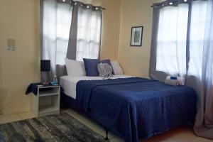 a bedroom with a bed with blue sheets and windows at An-Garo Ko-Zy Spaces in Saint Johnʼs