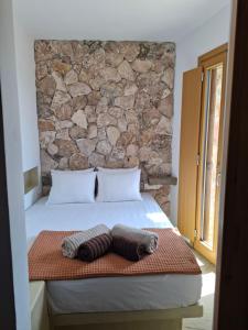 a bed with two pillows and a stone wall at ACHERONAS Residences in Serifos Chora