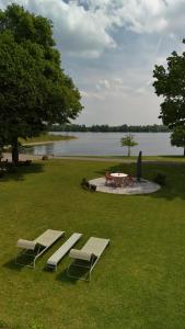 two lounge chairs and a table in the grass near a lake at Ferienwohnung Coproyshof - Direkt am See - 3 Schlafzimmer, privater Strand & Feuerstelle in Wesel
