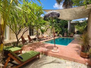 a pool with chairs and an umbrella next to a house at Nuik Casa Tropical in Mérida
