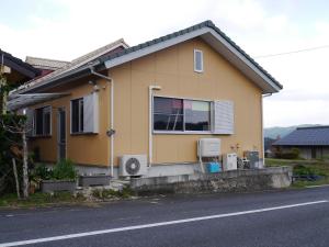una casa amarilla con 2 aparatos de aire acondicionado en una calle en Guest House Tomida en Ena