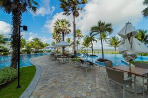 a resort pool with tables and chairs and palm trees at Apartamento a beira-mar com piscina in Cabedelo