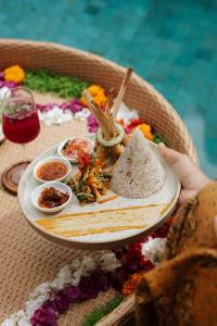 a person holding a plate of food on a table at Shankara D'Uma in Ubud