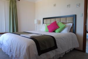 a bedroom with a large bed with green and pink pillows at Oceana Sunset in Warnbro