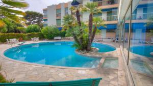 Una piscina con palmeras y un edificio. en Eden Park 3 pièces 4 étoiles 100m des Plages Piscines SPA Parking, en Cannes