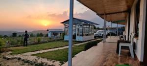 a man standing on the porch of a house with the sunset at Sunshine Cottages in Bīr
