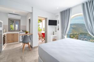 a white bedroom with a large window and a kitchen at Epsilon Apartments in Kalymnos