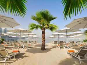 a beach with chairs and a palm tree and umbrellas at Adagio Premium The Palm in Dubai