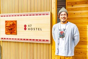 a man standing in front of a building with a sign at 47HOSTEL in Wadomari
