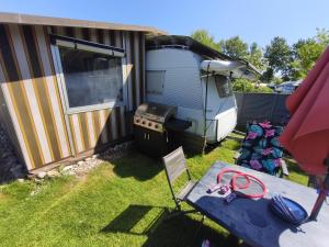 a picnic table next to a trailer with a grill at Wohnwagen mit feststehendem Vorzelt in Fehmarn