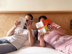 a man and woman laying in bed reading books at Greet Hotel Colmar in Colmar