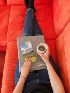 a woman sitting on a couch with a book and a cup of coffee at Pension Schachner in Schladming