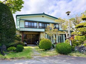 a large house with a green roof and bushes at Yabukiso in Yamanakako