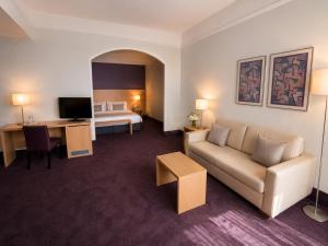 a hotel room with a couch and a desk and a bed at guestified GRAND AIRPORT Hotel Düsseldorf Ratingen in Ratingen