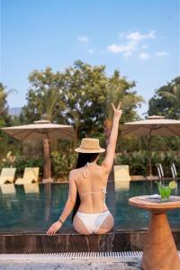 a woman in a bikini sitting next to a pool at Rivana Retreat in Sóc Sơn